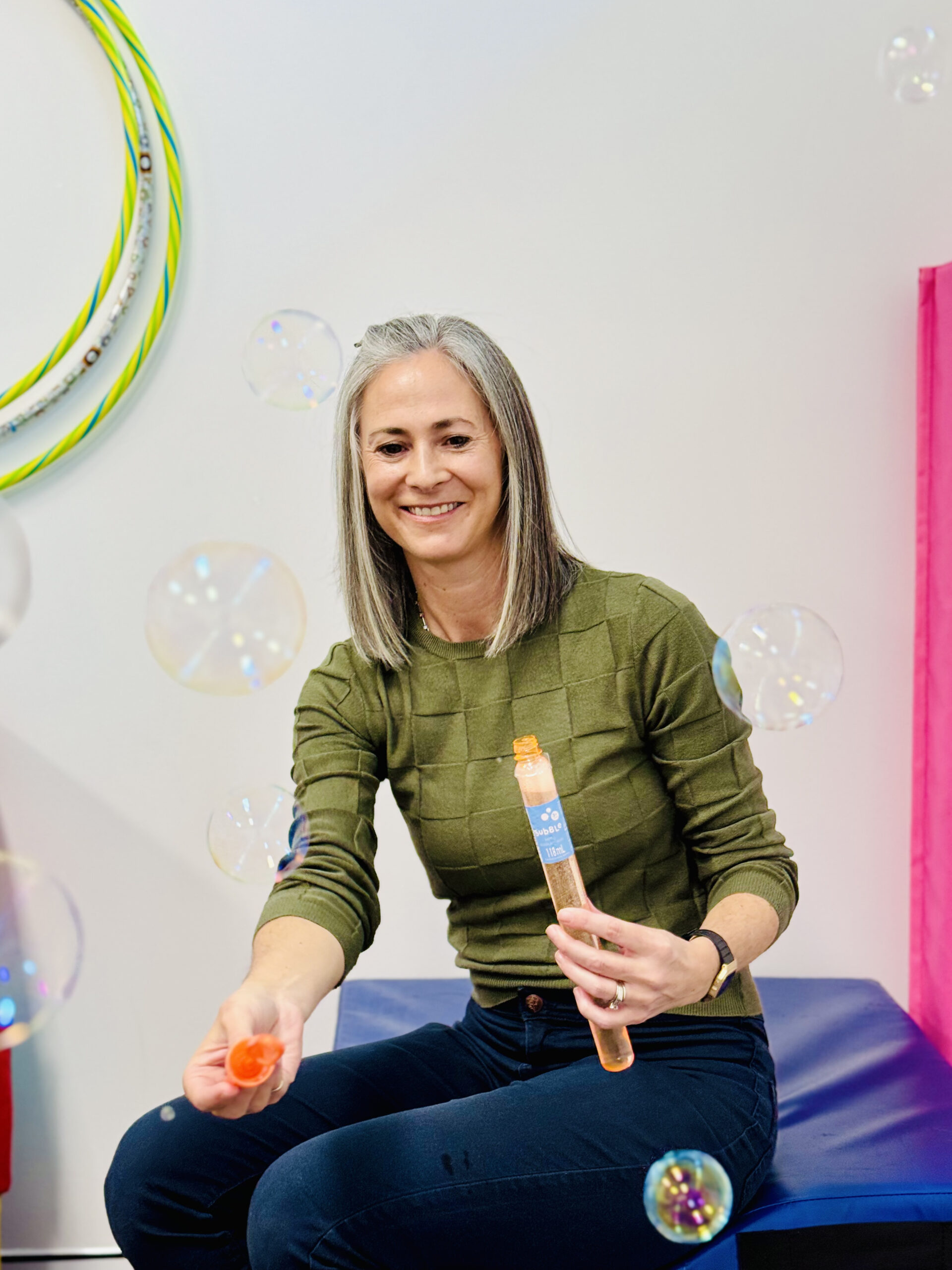 A woman sits on a bench, surrounded by floating bubbles, enjoying a serene moment outdoors.