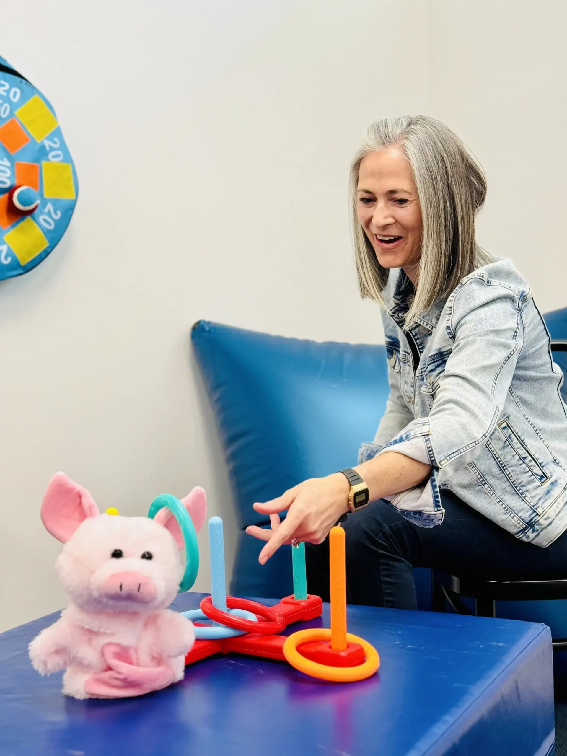 A woman joyfully interacts with a toy pig on a table, showcasing a playful moment in a cozy setting.