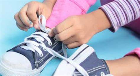 A child kneels down, focused on tying the shoelaces of a bright pair of sneakers.