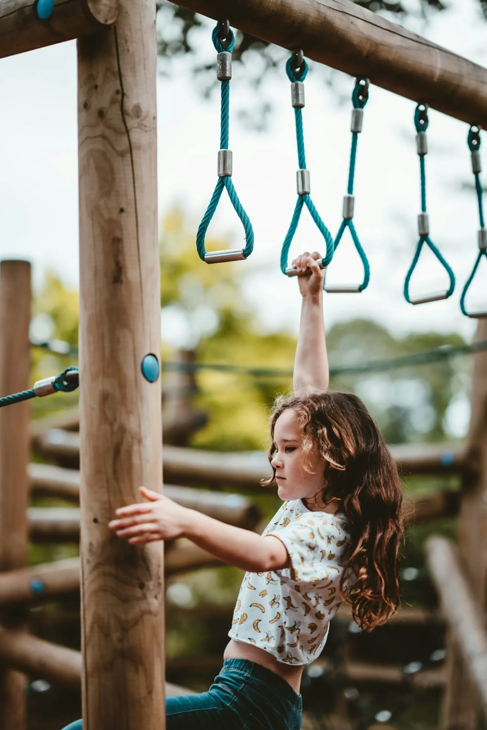 A young girl skillfully climbs a wooden playground structure, showcasing her adventurous spirit and playful nature.
