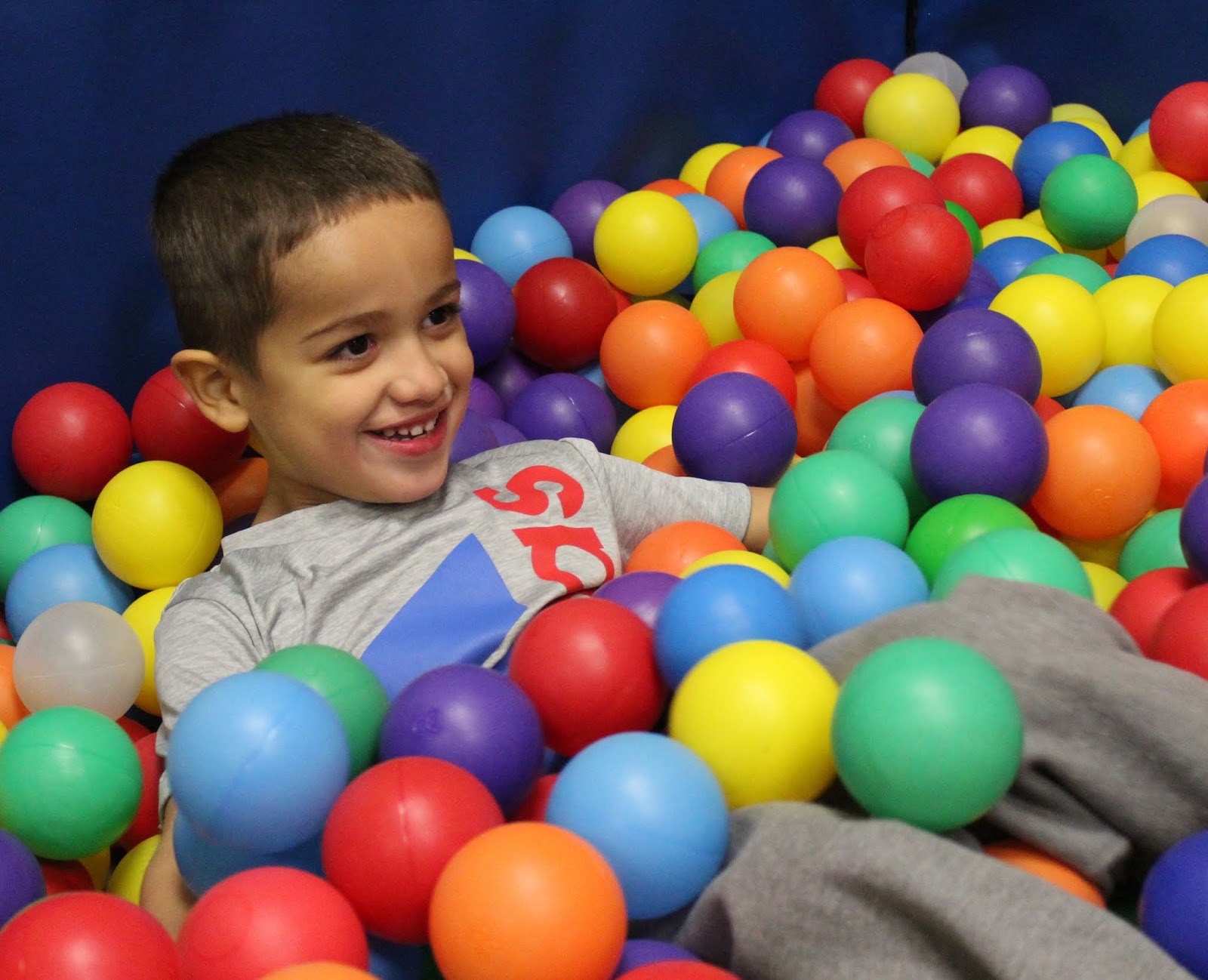 A young boy smiles joyfully while sitting amidst colorful balls in a vibrant ball pit.